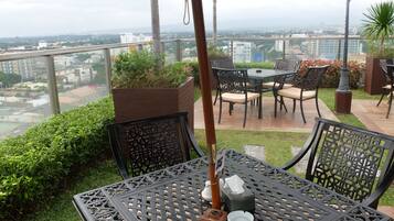 Um pátio externo com mesa e cadeiras, um vaso com flores e vista para o horizonte urbano.