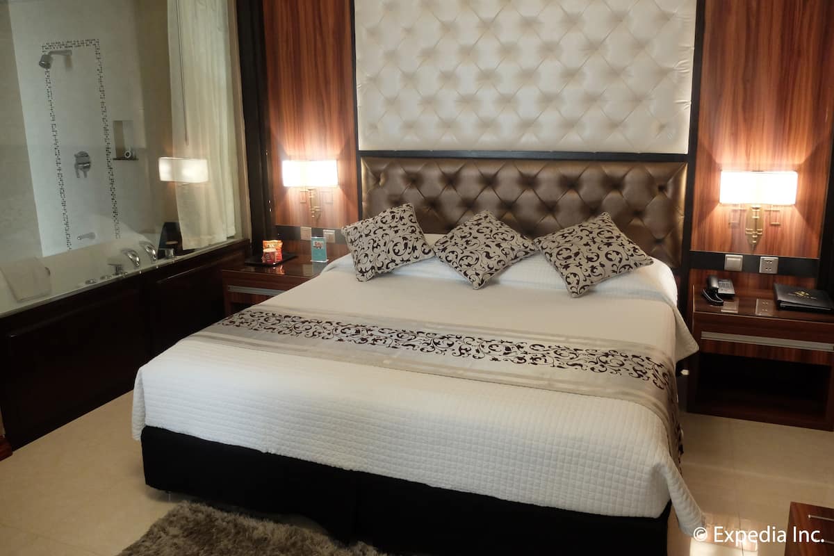 Ein Hotelzimmer mit einem großen Bett, einem Spiegel, einem Nachttisch, einer Lampe und einem Badezimmer mit Dusche.