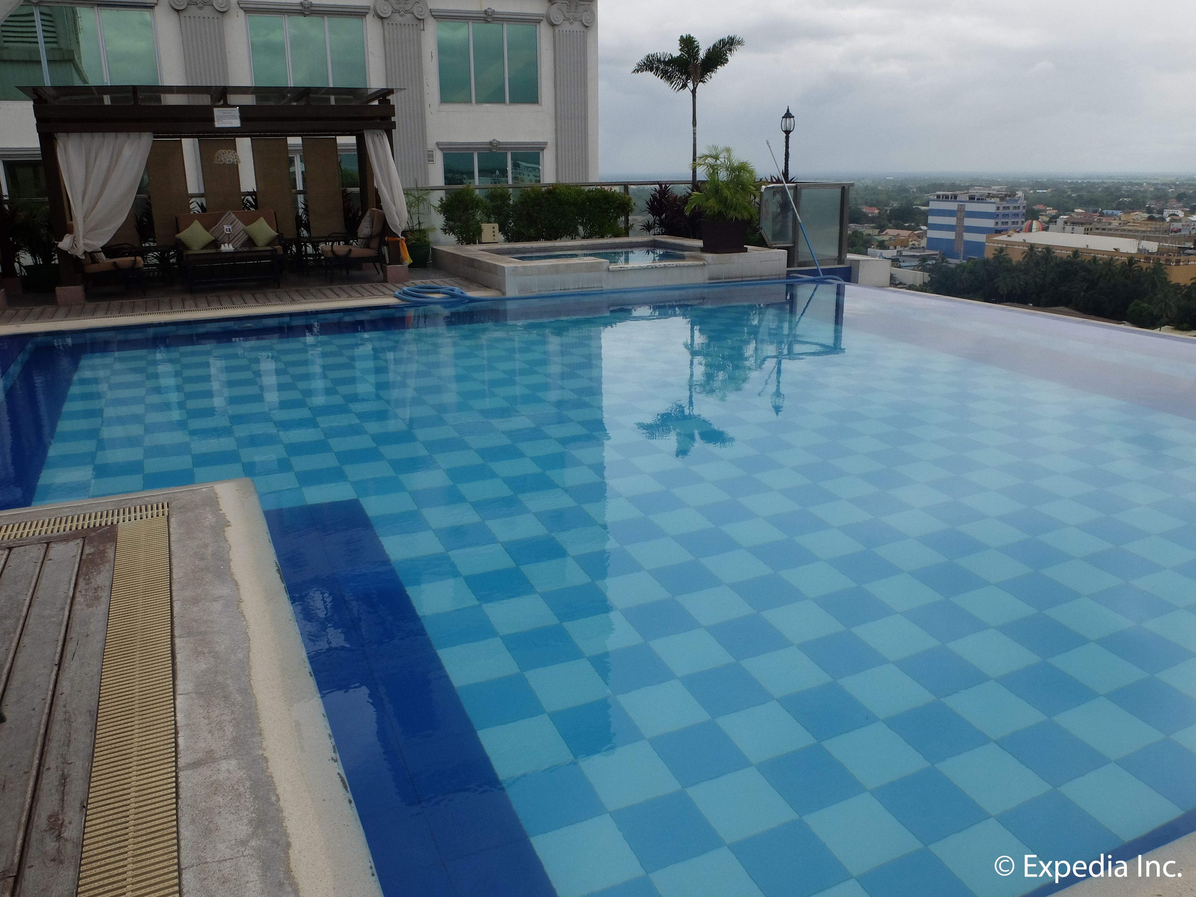 A pool with a checkered pattern, a pergola with seating, and a view of the cityscape in the background.