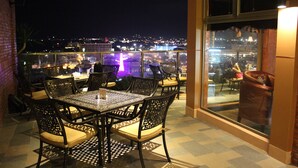 Een terras op het dak met een tafel en stoelen, met uitzicht op een stadsbeeld bij nacht.