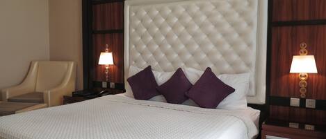 Una habitación de hotel con una cama grande, un cabecero, dos mesitas de noche, una silla y dos lámparas de pared.