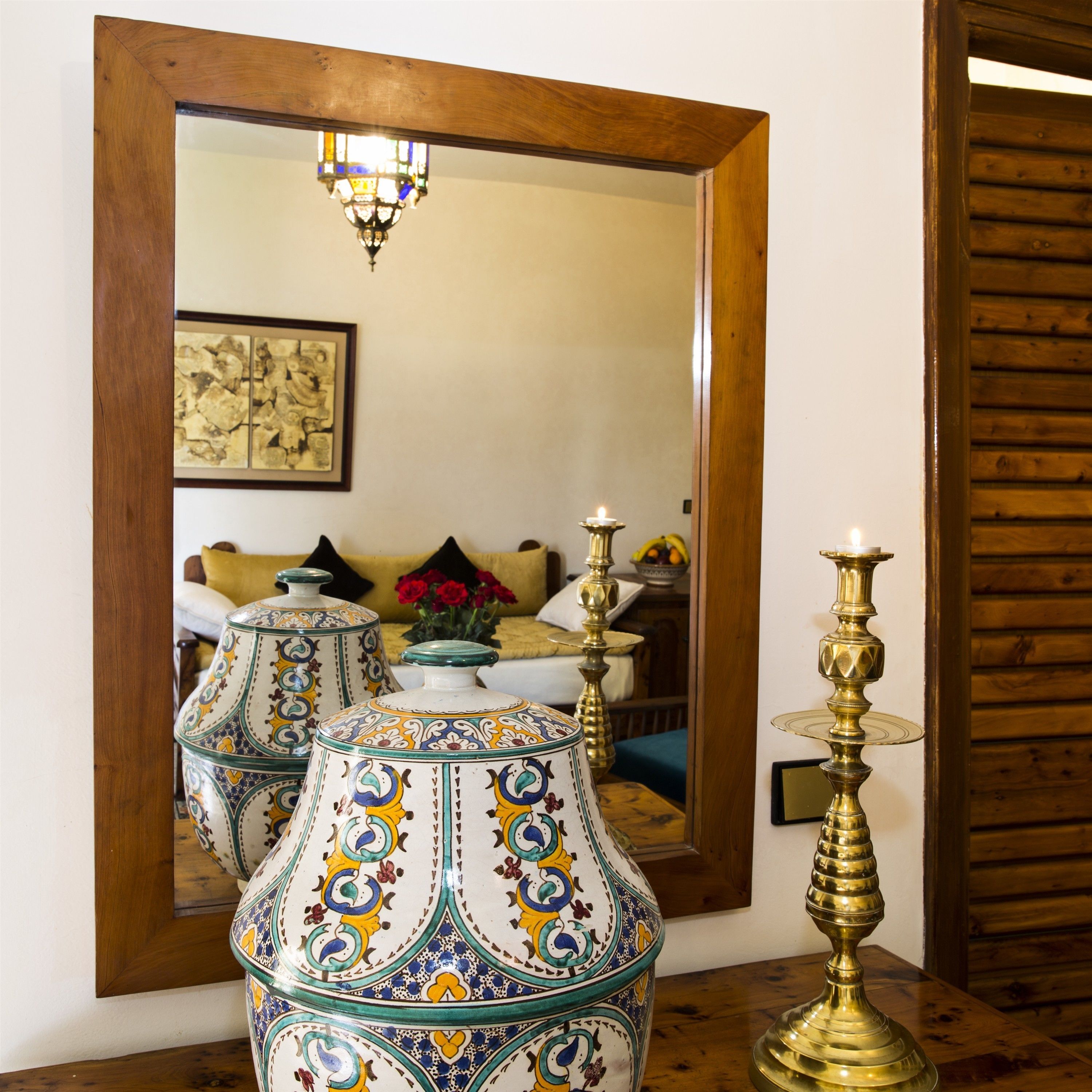 A room with a large mirror reflecting a chandelier, a decorative vase, and a candelabra.