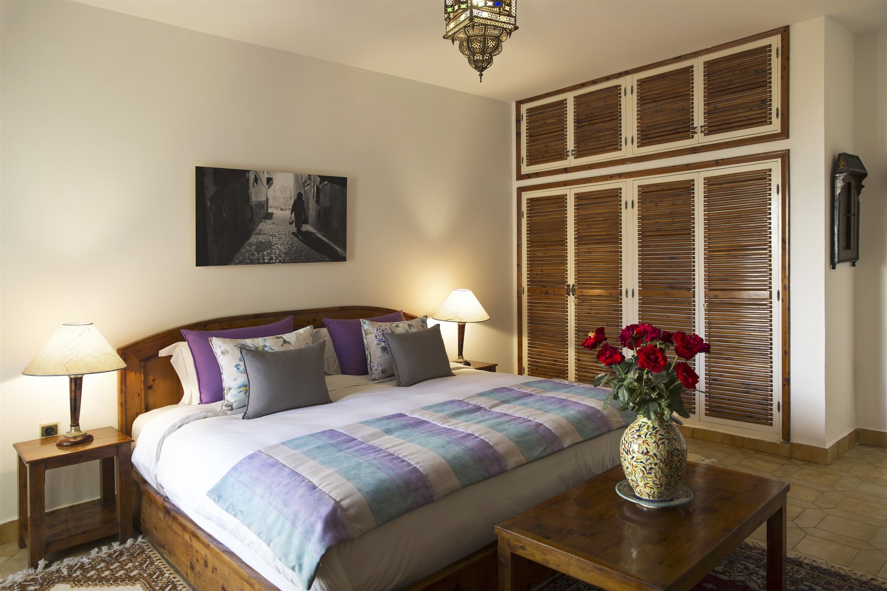 Une chambre à coucher comprenant un lit, deux tables de chevet avec des lampes, une commode, une grande armoire en bois et une horloge murale.