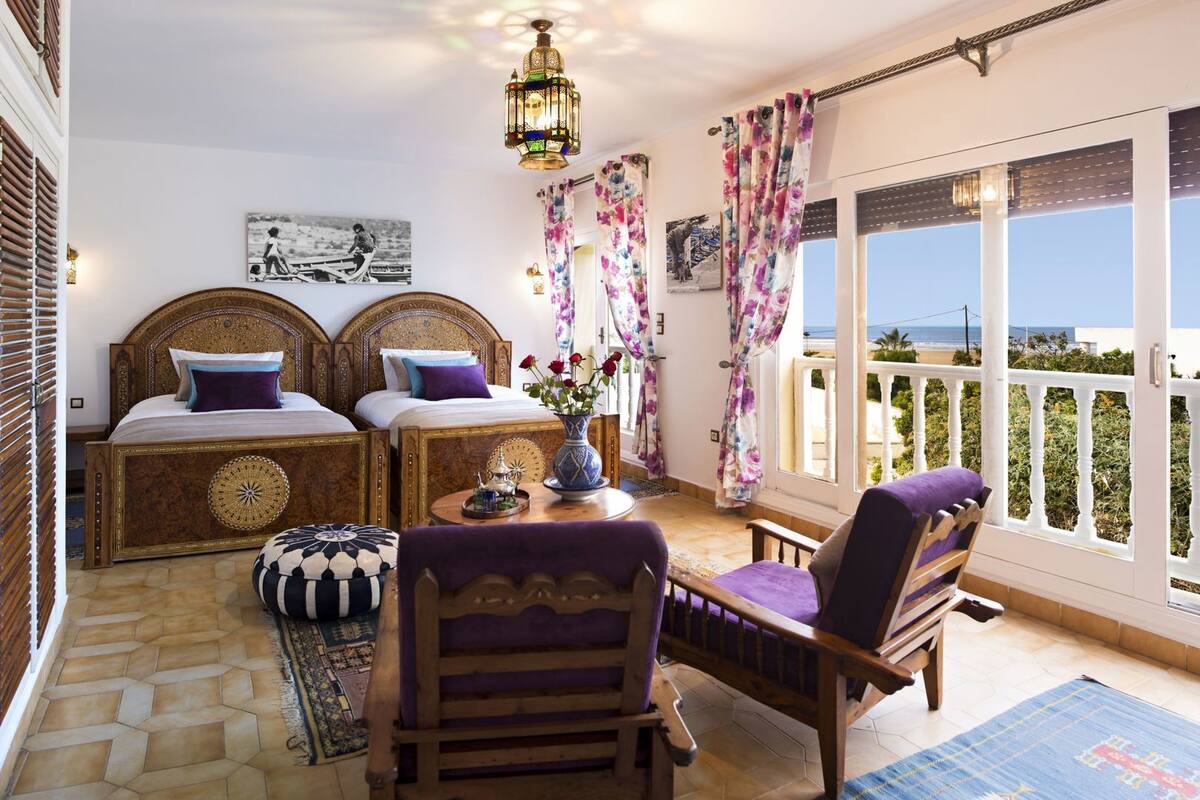 A bedroom with two beds, a balcony with a view, and a dining area with a table and chairs.