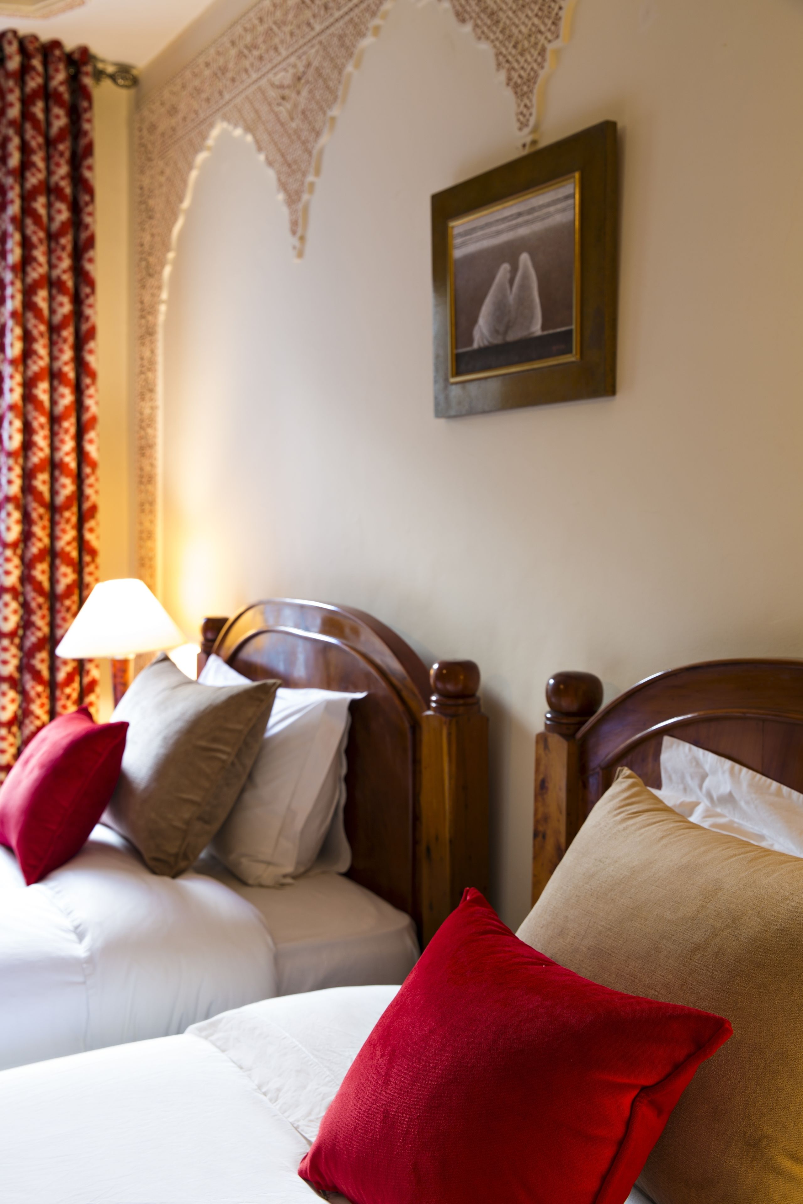 A hotel room with two wooden beds, each with a red and beige pillow. A framed picture hangs on the wall above the beds.