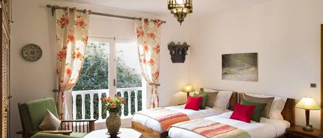 Une chambre avec deux lits, un balcon, une chaise en bois, une table avec un vase et un luminaire suspendu.
