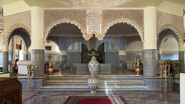 Una habitación con detalles intrincados en mosaicos, arcos y un jarrón ornamentado en el centro.