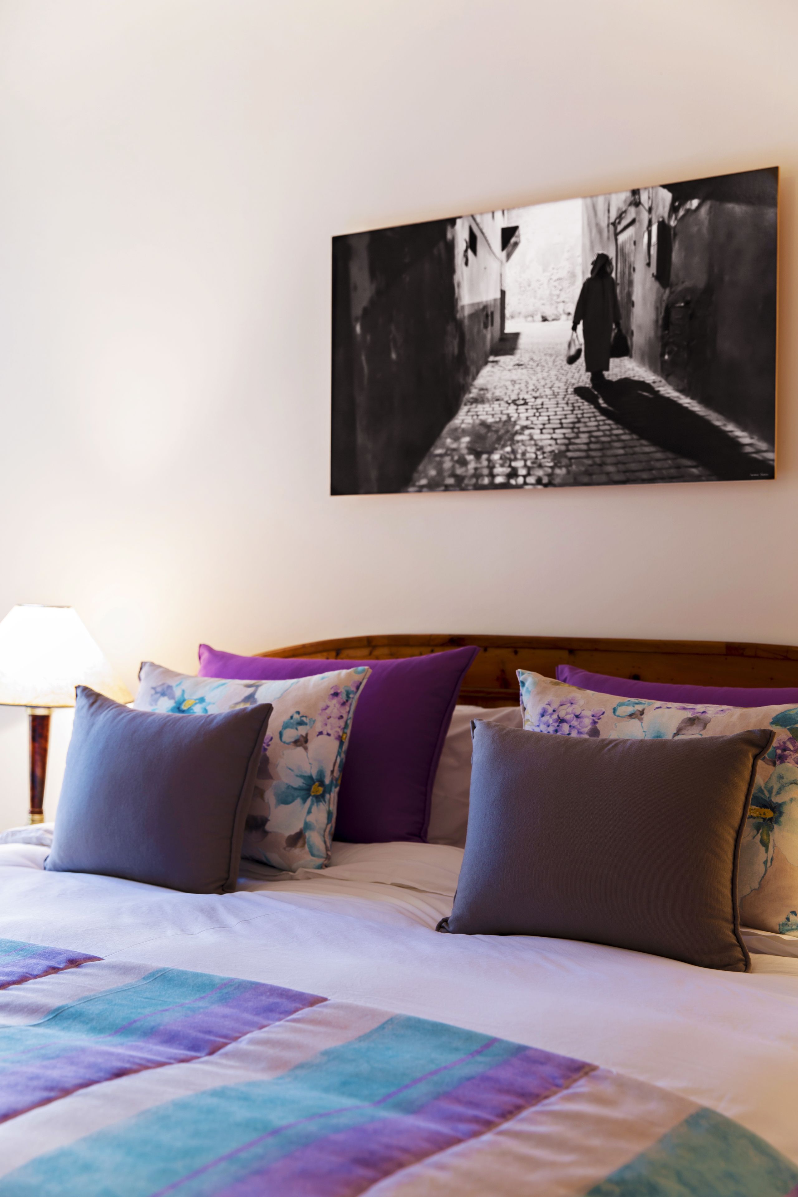 A neatly made bed with a colorful quilt, a wooden headboard, and a black and white photograph of a street scene above it.