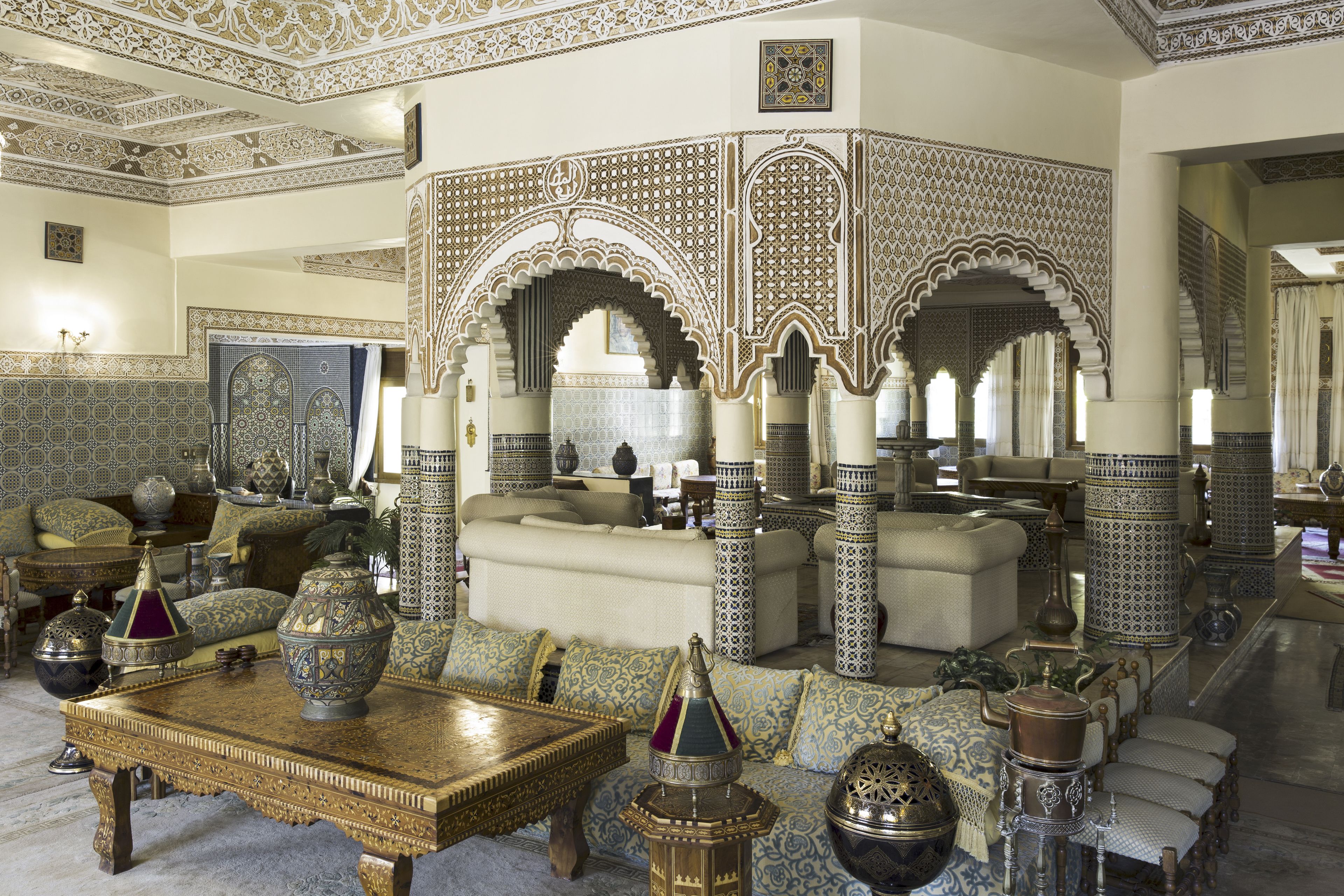 A traditional Moroccan interior with ornate arches, a central seating area, and a variety of decorative items.