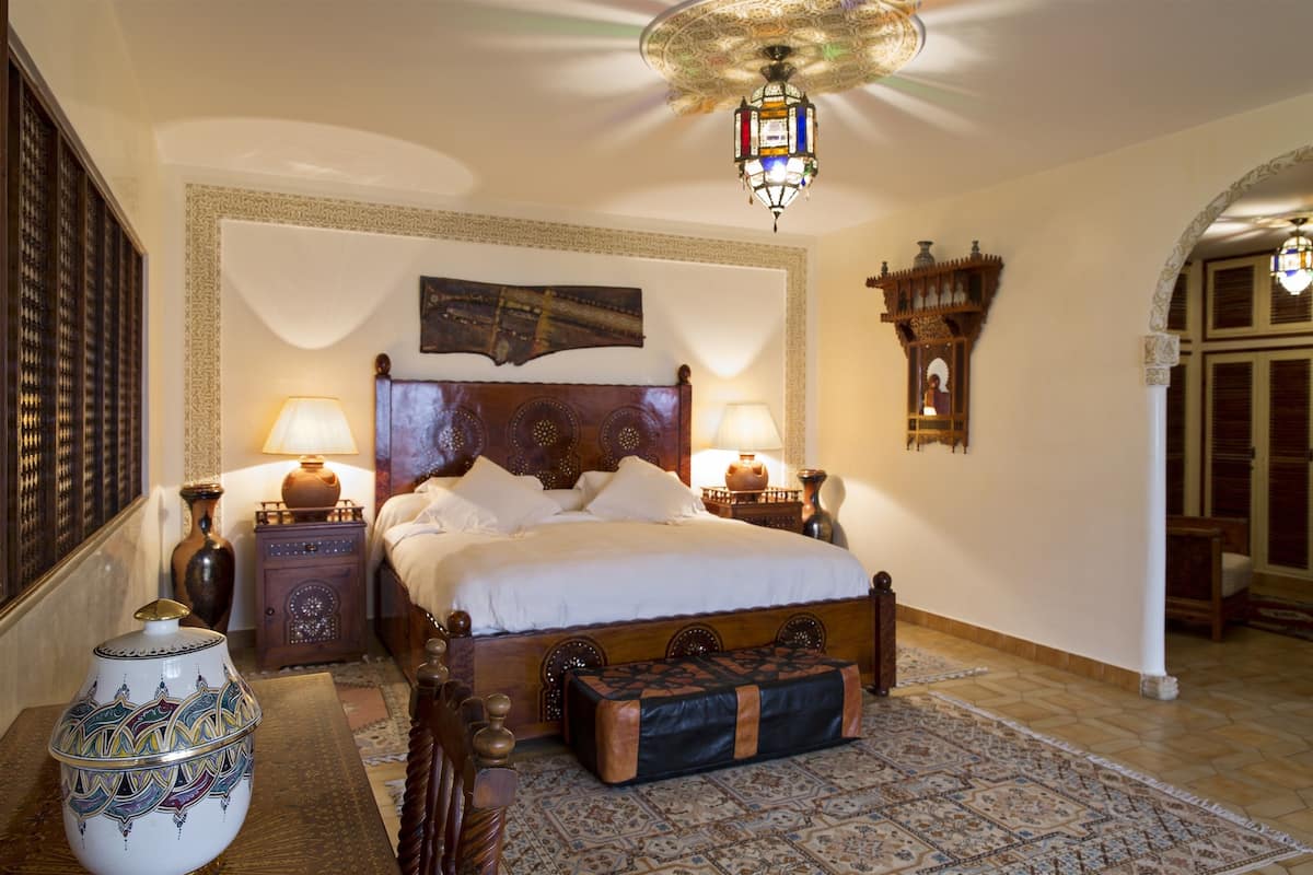 A traditional room with a large bed, two bedside tables with lamps, a decorative wall hanging, and a patterned rug.