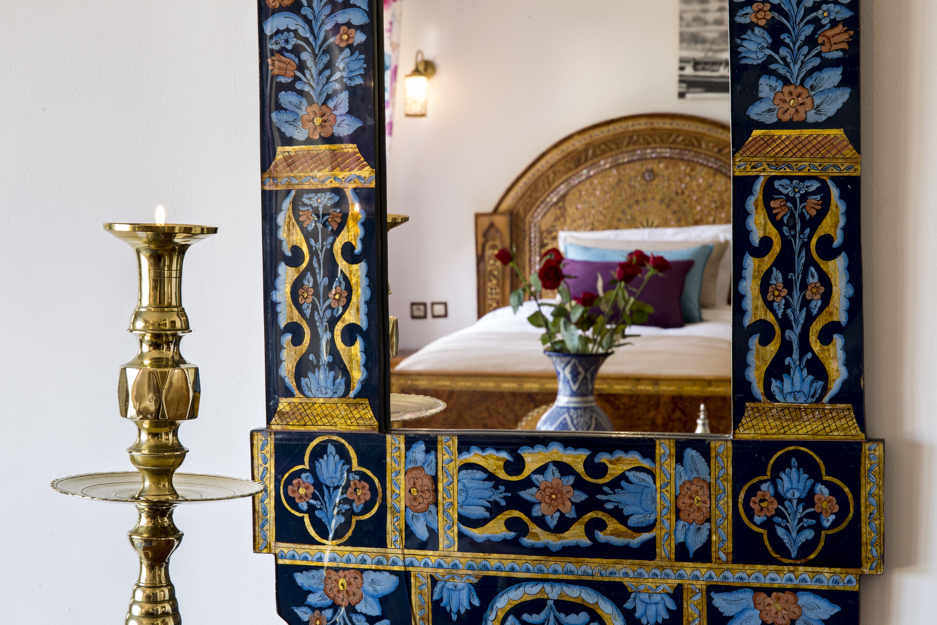 A room with a bed, a decorative mirror, and a brass lamp.