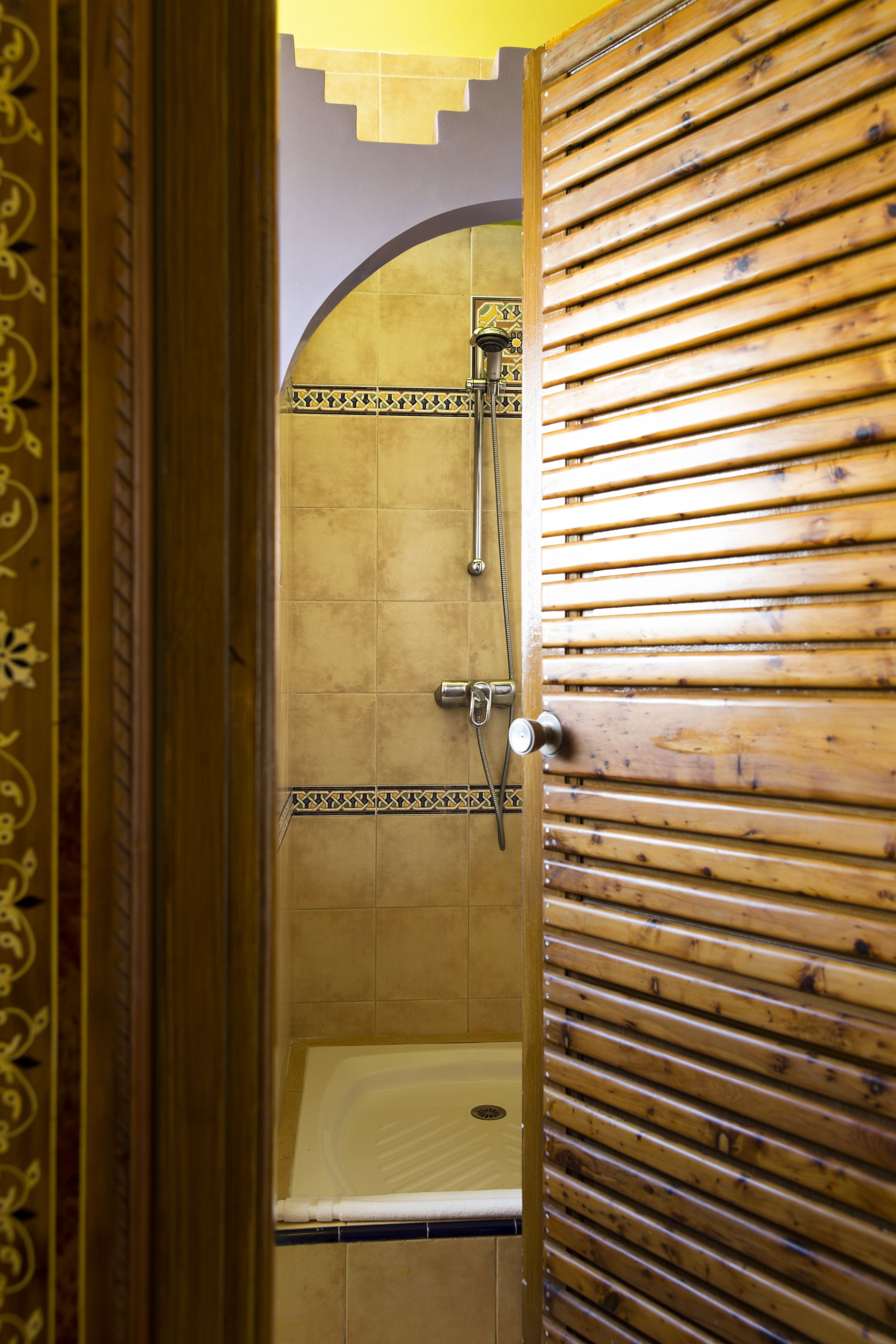 Une salle de bain avec une porte en bois, une douche et un sol carrelé.