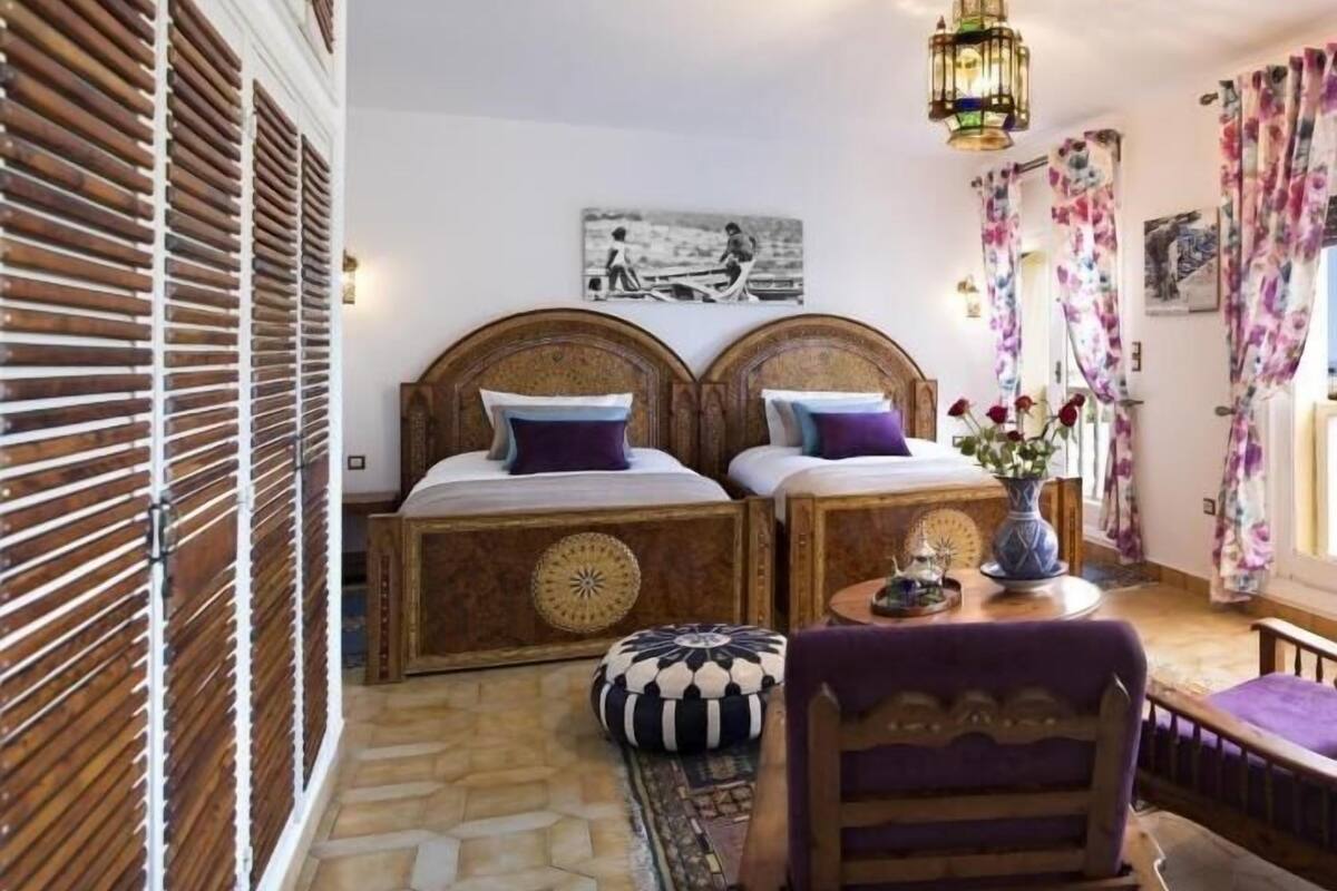 A room with two wooden beds, a patterned rug, a wooden chair, and a hanging lantern.