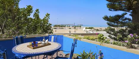 A blue-tiled outdoor seating area with a table and chairs, overlooking a beach and palm trees.