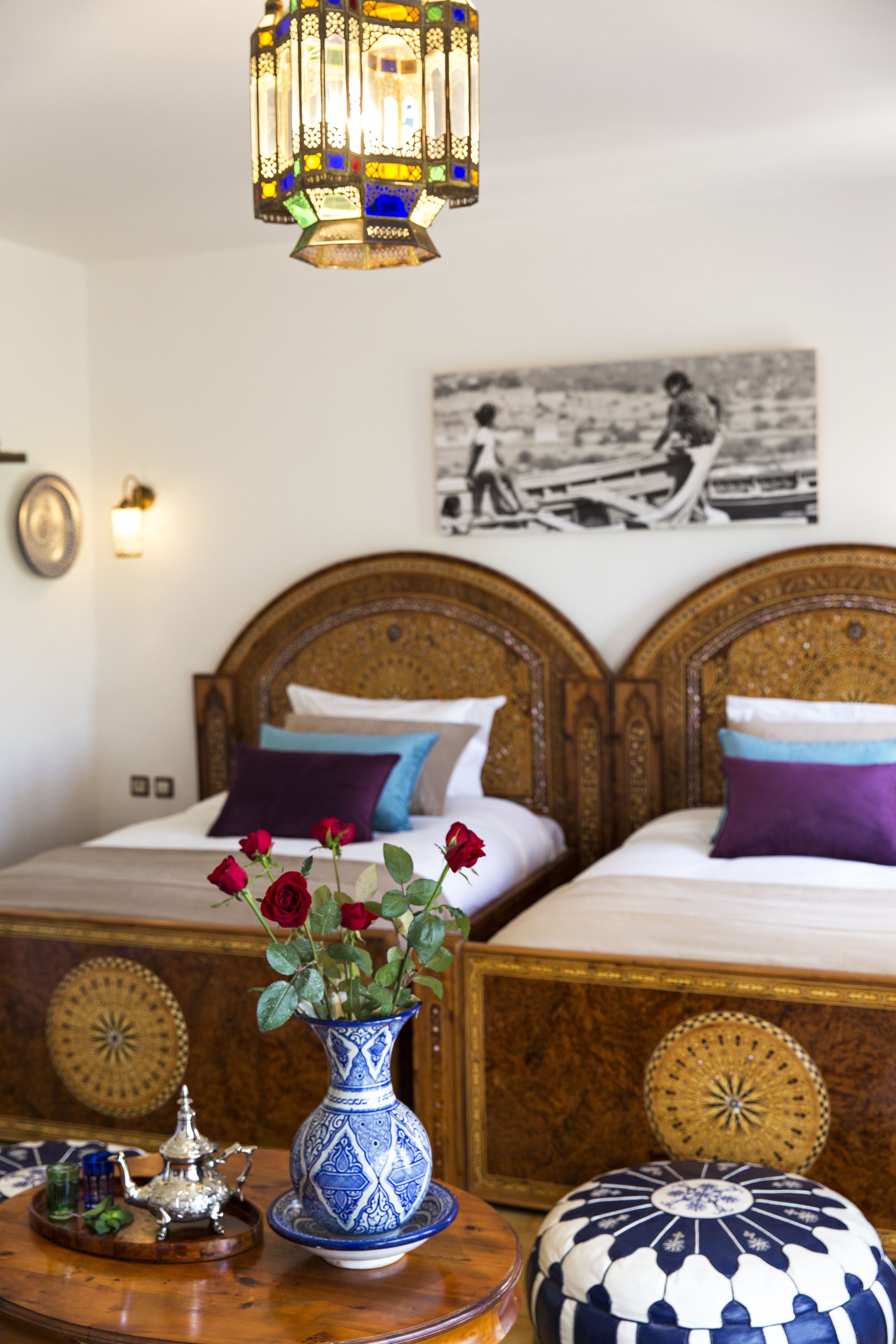 Een slaapkamer met twee bedden, een decoratieve vaas met bloemen, een tafel met theepot en een hanglamp.