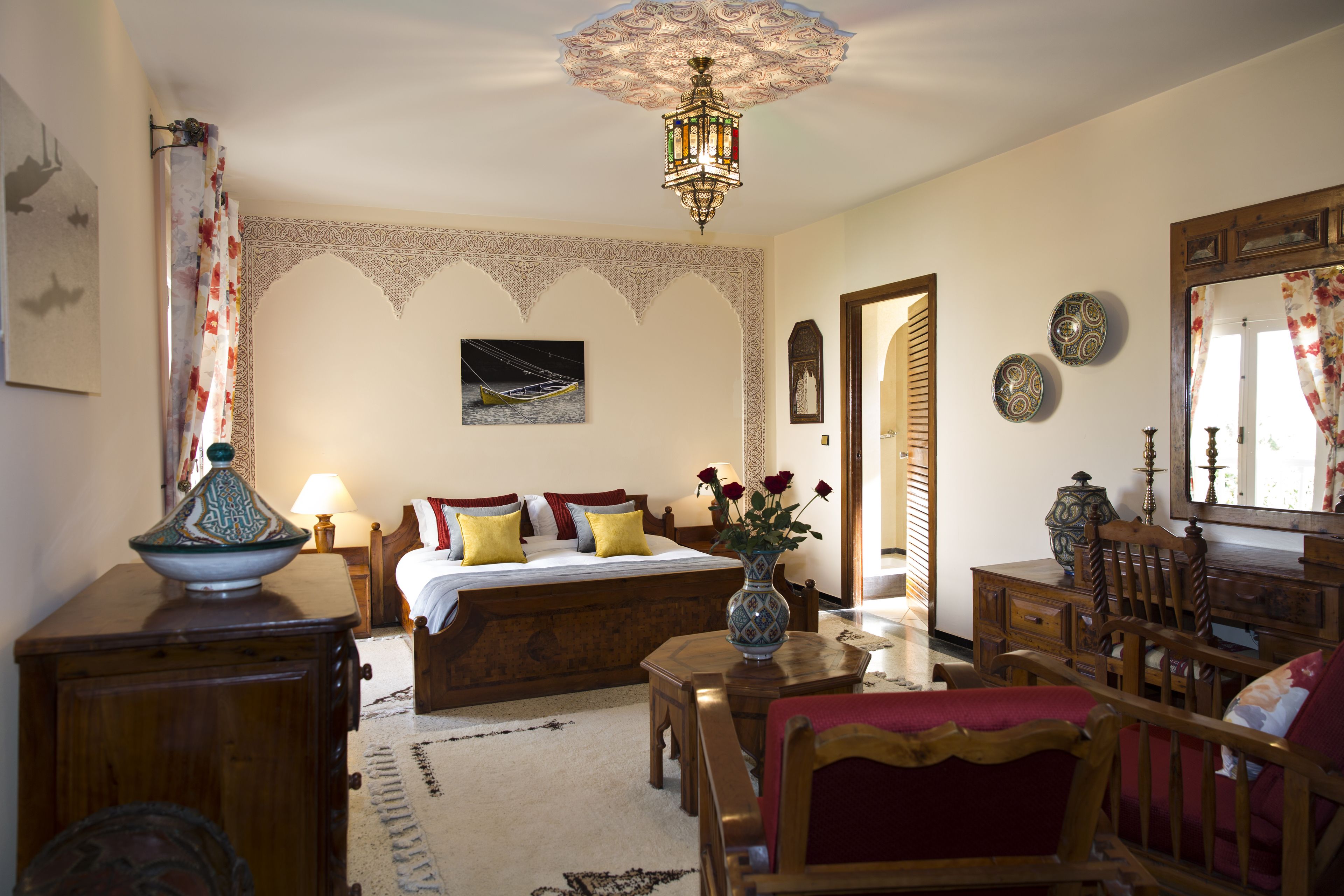 A traditional bedroom with a bed, bedside table, lamp, and a decorative vase with flowers.