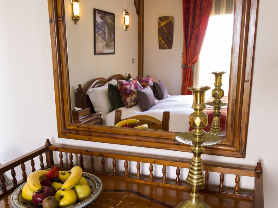 A room with a bed, a mirror, a bowl of fruit, and a brass candelabra.