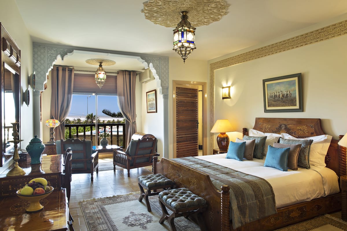 A spacious bedroom with a large bed, a balcony view, ornate ceiling, and traditional decor.