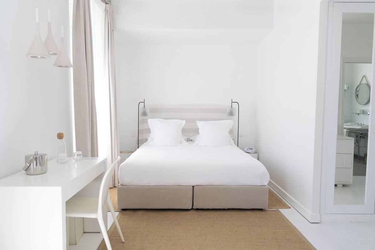 Een minimalistisch hotelkamer met een bed, nachtkastje en bureau met stoel.