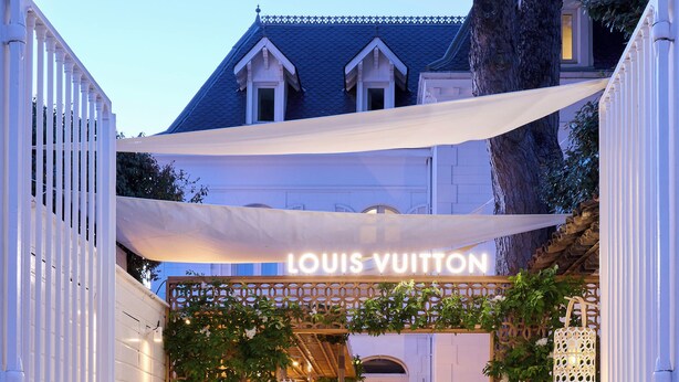 Entrada a una tienda Louis Vuitton con fachada de madera, paneles de celosía blanca y un toldo.