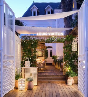 Entrada a una tienda Louis Vuitton con fachada de madera, paneles de celosía blanca y un toldo.