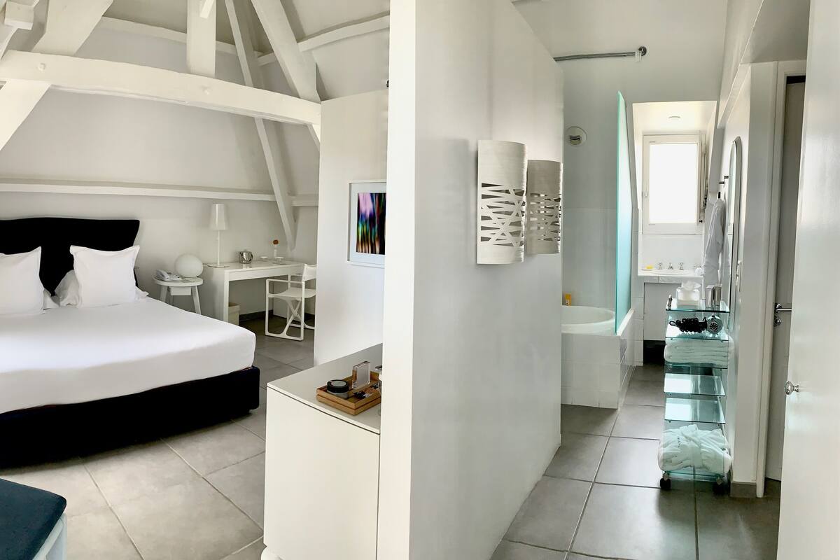Een moderne hotelkamer met een bed, een bureau, een stoel en een badkamer met een douchecabine van glas.