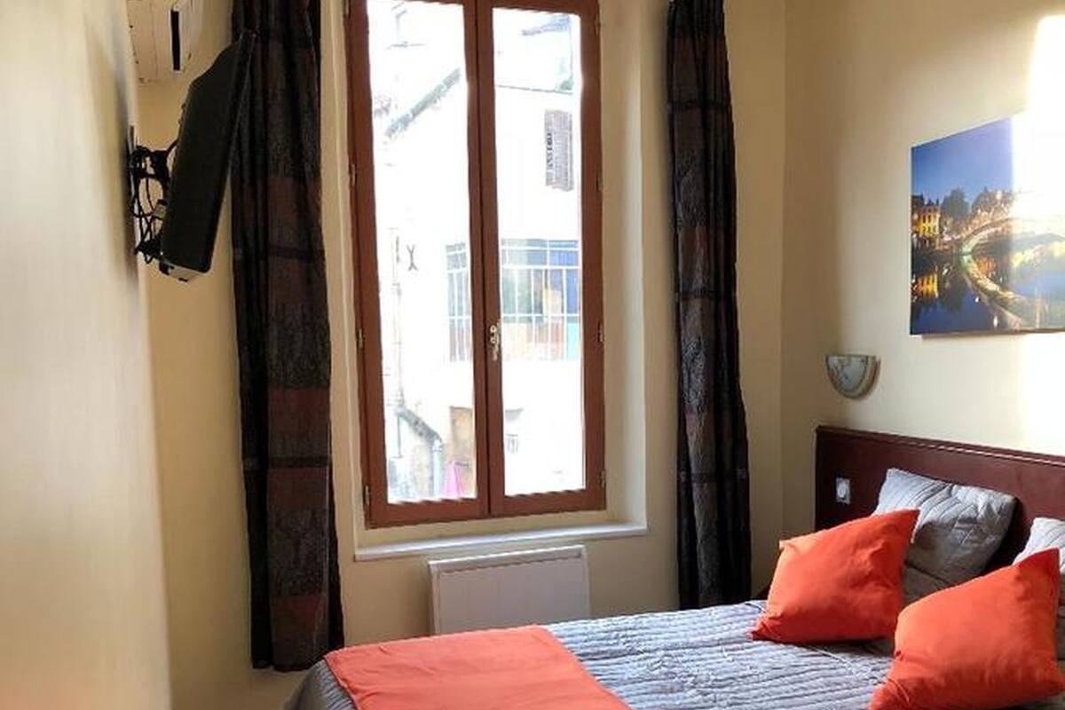A bedroom with a bed, a window, a wall-mounted air conditioner, and a painting.