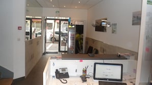 A reception desk with a computer, phone, and various office supplies. - Hôtel Victory (Marseille)