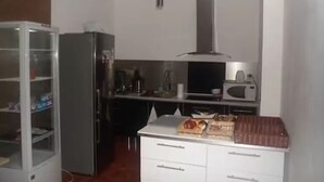 A compact kitchen with a refrigerator, microwave, and a small dining area with a table and chairs. - Hôtel Victory (Marseille)