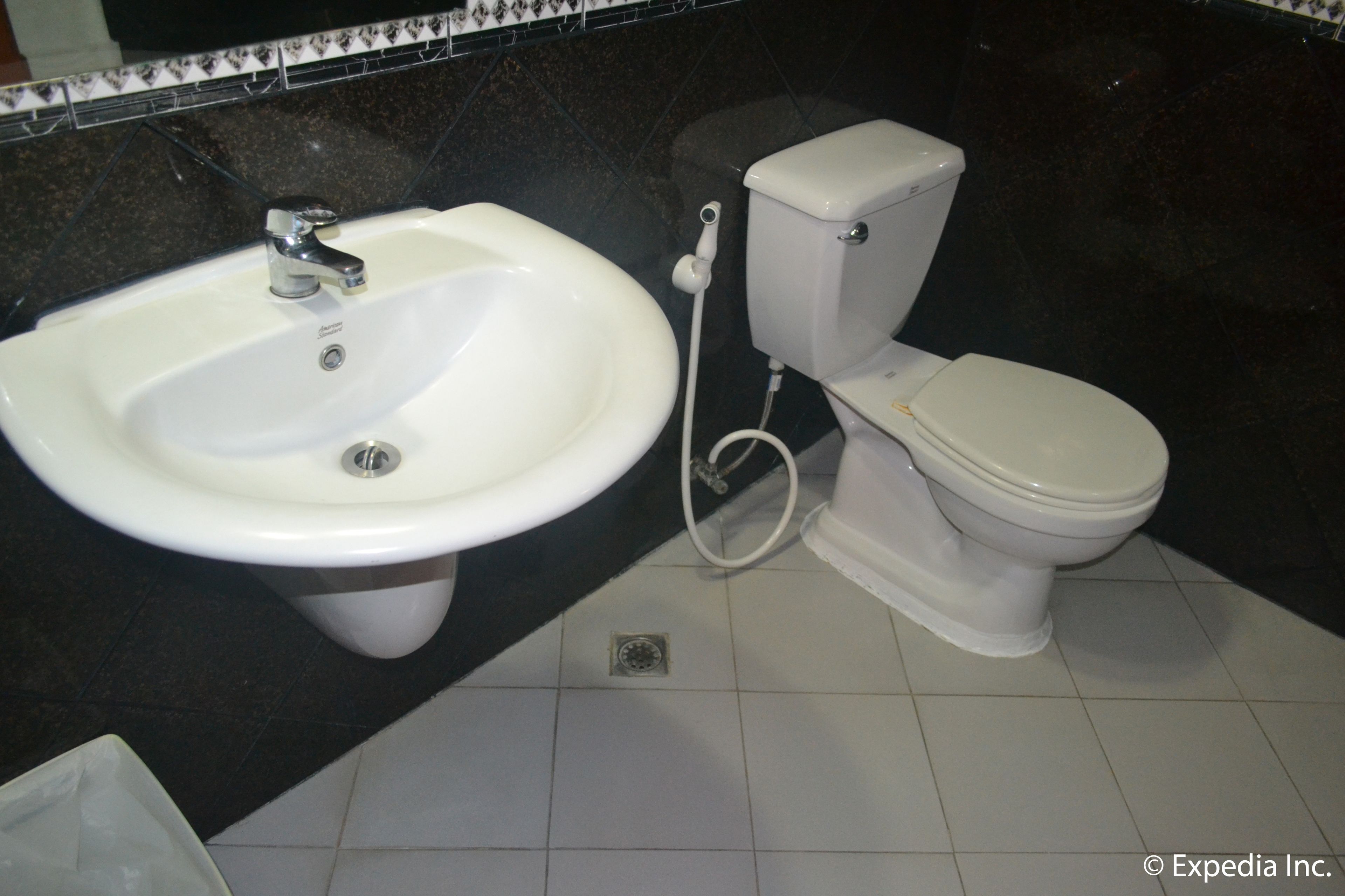 Ein Badezimmer mit weißem Waschbecken und WC, schwarzen Fliesenwänden und einem gefliesten Boden.