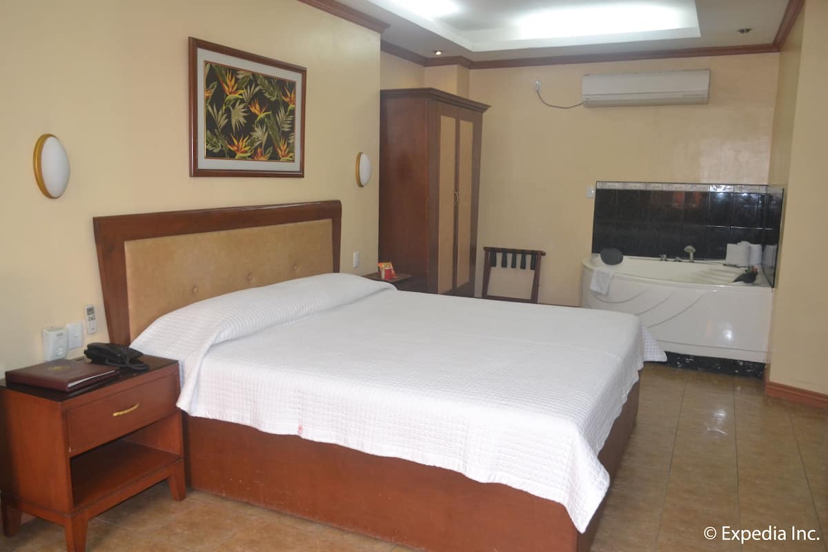 Habitación de hotel con una cama grande, una mesita de noche, un armario, un baño con bañera y un aire acondicionado instalado en la pared.