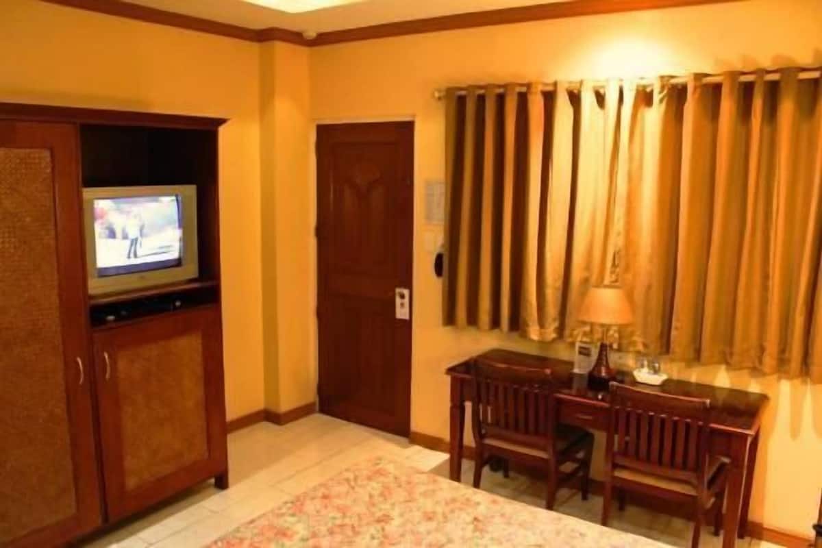 Una habitación de hotel con televisión, un escritorio con sillas, una lámpara y un ventanal con cortinas.