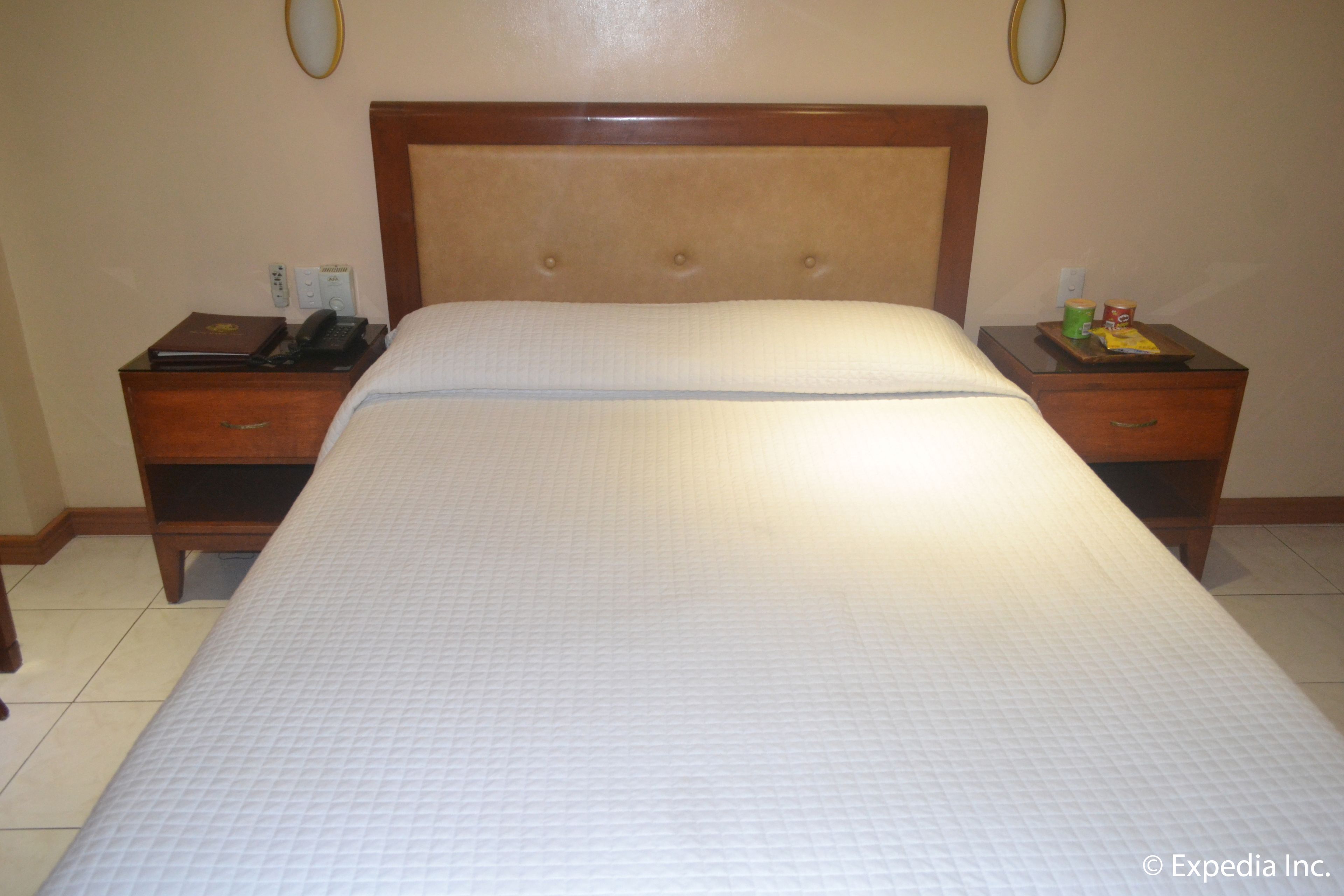 Una habitación de hotel con una cama grande, cabecera de madera, dos mesitas de noche y un atril con un teléfono y un libro.