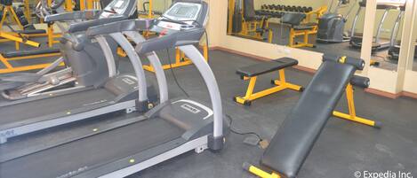 Un gimnasio con cintas de correr, máquinas de pesas y bancos.