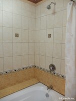 Baño con bañera, ducha y paredes de azulejos.
