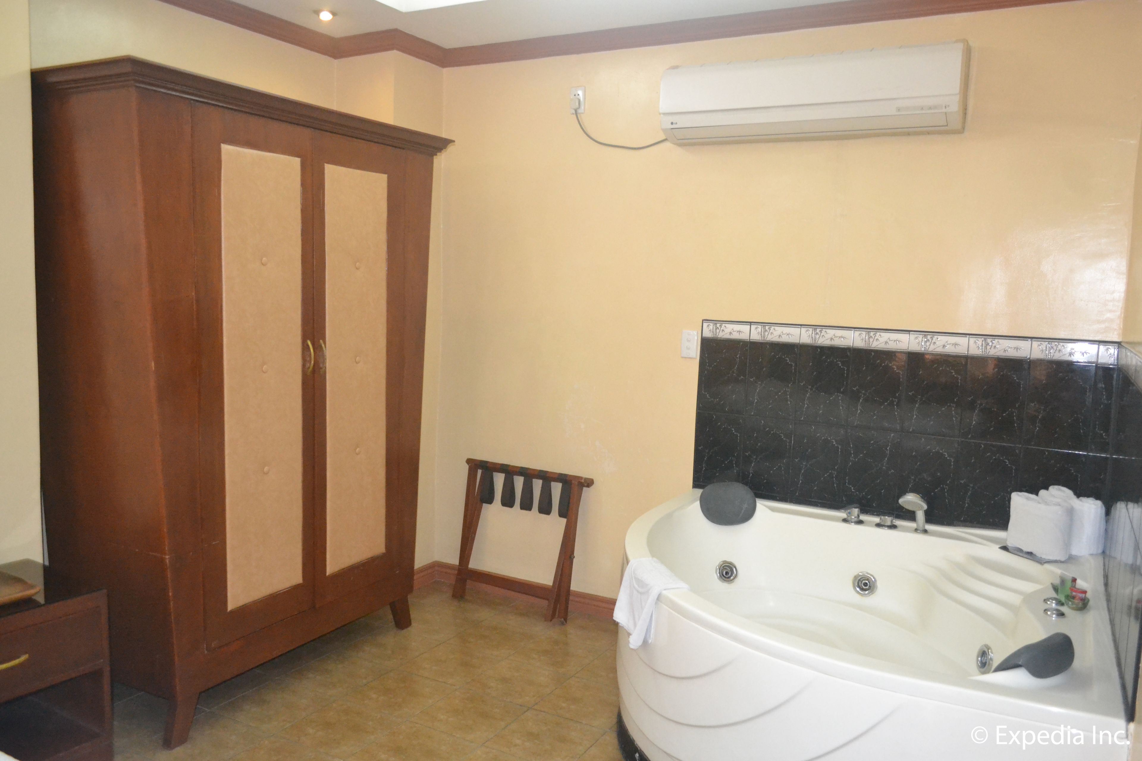 Un baño con un amplio armario de madera, un pequeño taburete y una bañera grande con un resalte de mármol negro.
