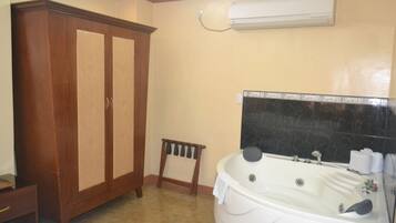 Un baño con un amplio armario de madera, un pequeño taburete y una bañera grande con un resalte de mármol negro.