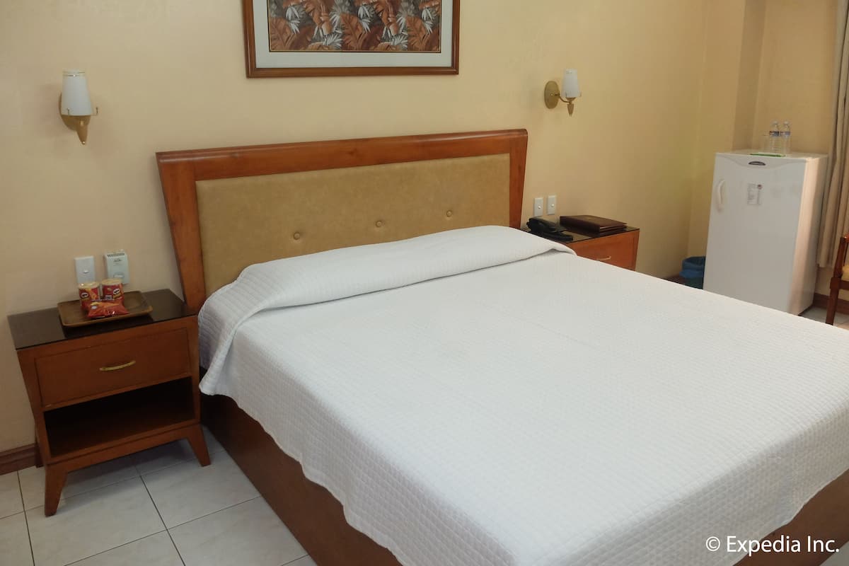 Una habitación de hotel con cama, mesita de noche, lámpara, decoración en la pared y un refrigerador.