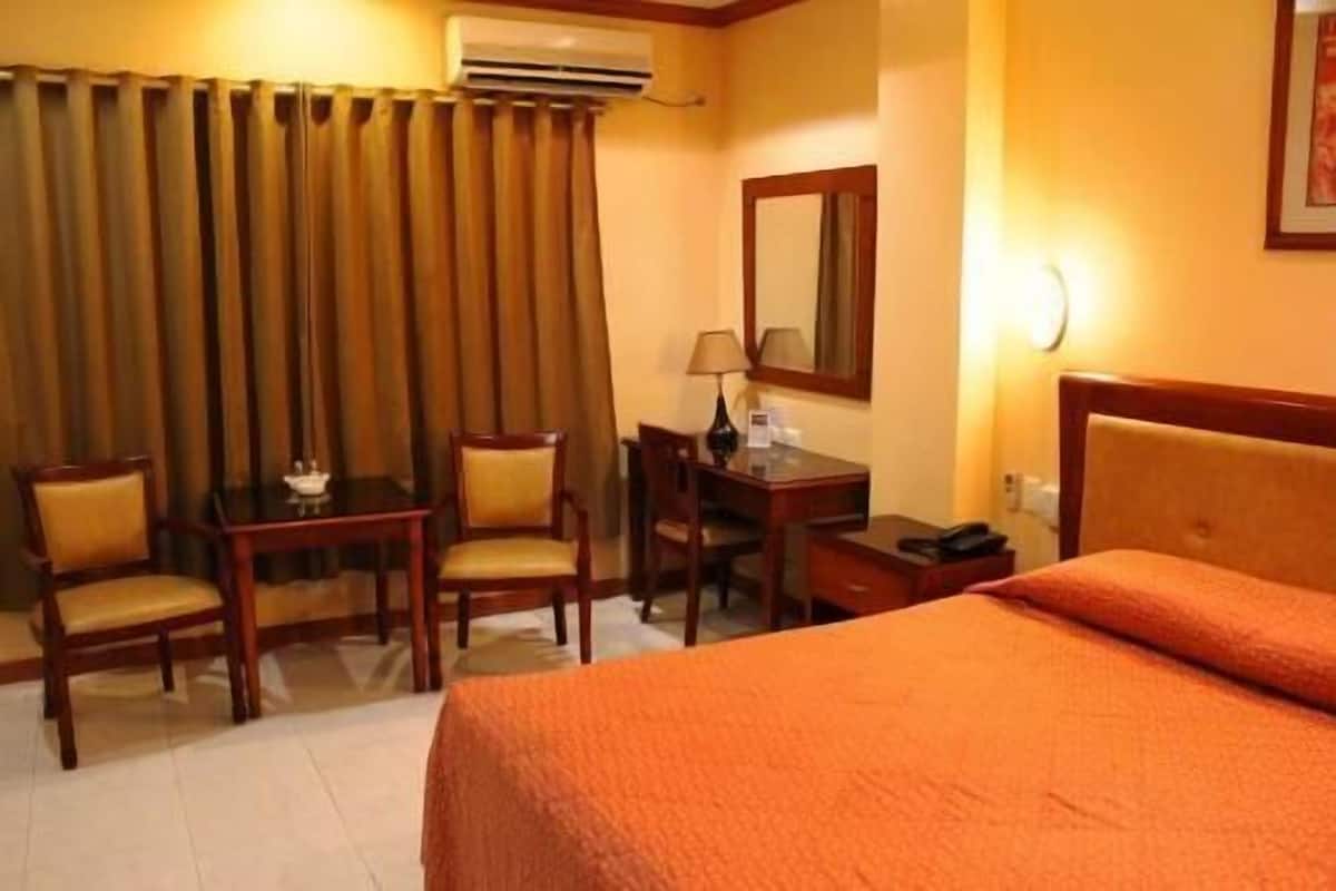 Habitación de hotel con cama, escritorio, dos sillas, lámpara y equipo de aire acondicionado.