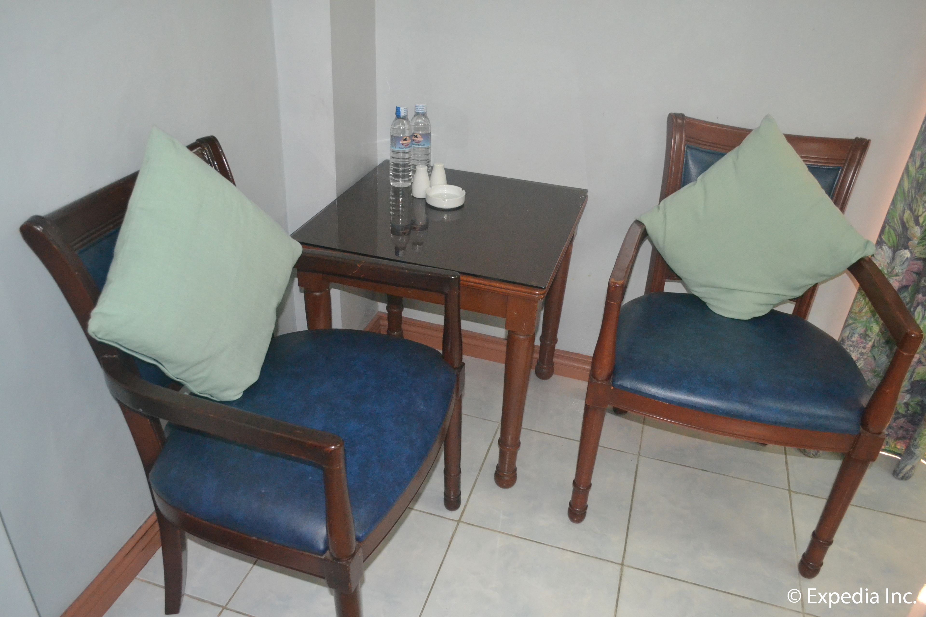 Un petit coin repas avec deux chaises en bois et une table, chacune agrémentée d’un coussin. Sur la table, on trouve deux bouteilles et un petit bol blanc.