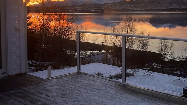 Una terraza con vistas a un lago y montañas al atardecer.