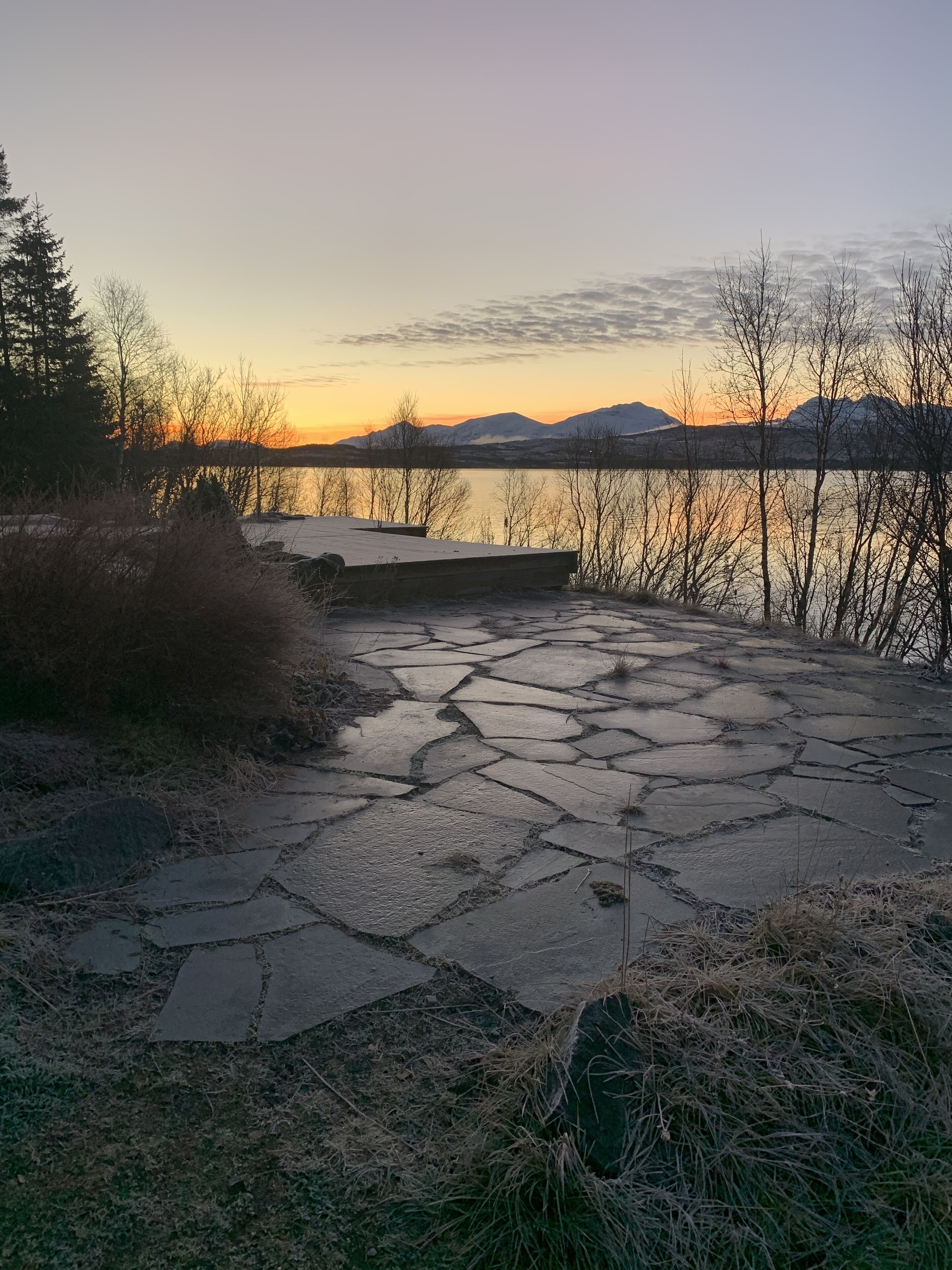 A stone pathway leading to a dock by a lake with mountains in the background.