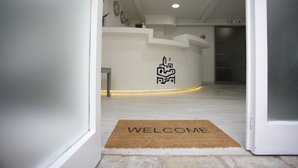 Uma área de recepção moderna com tapete de boas-vindas, uma placa na parede e uma escadaria para um andar superior.