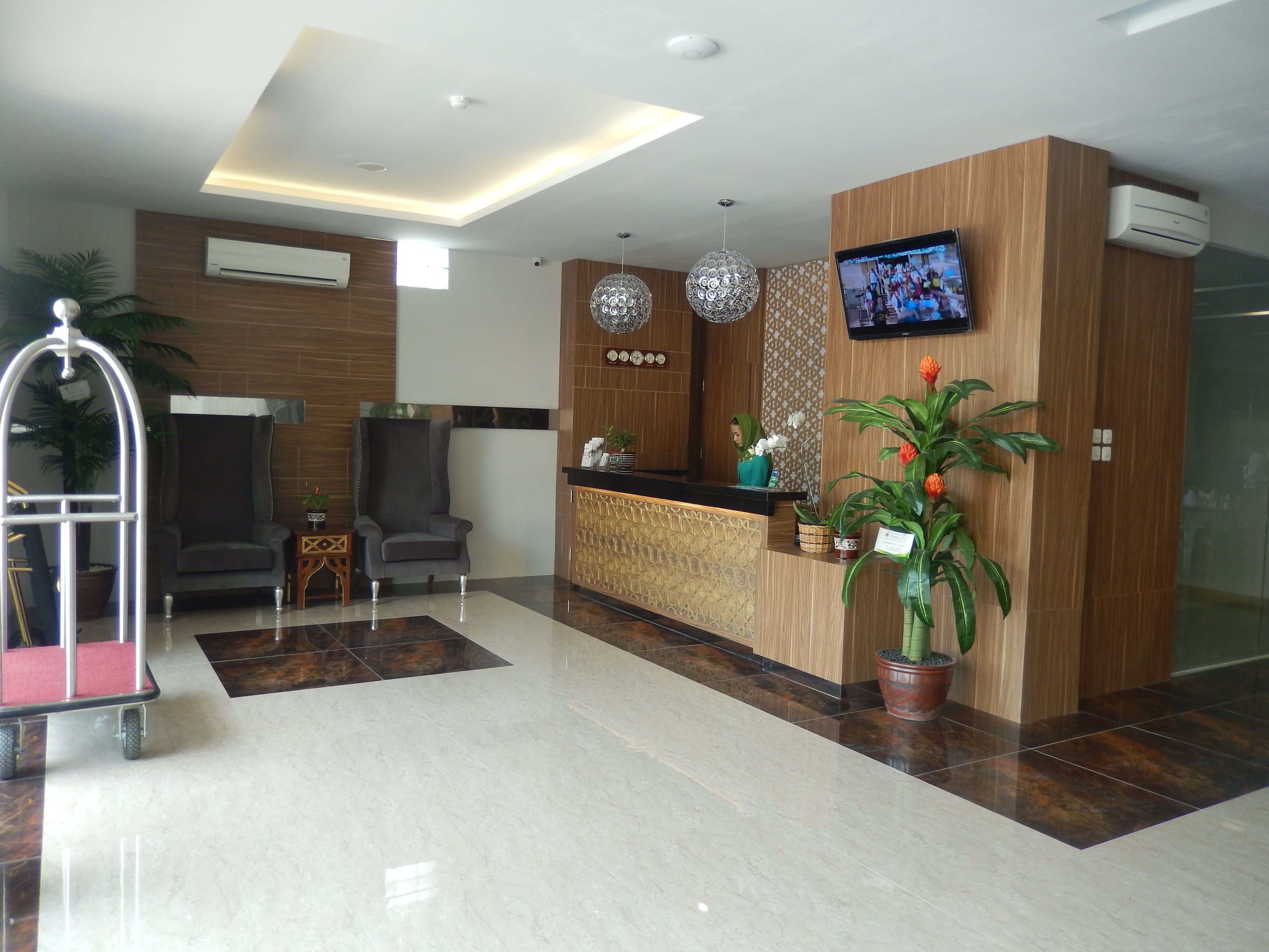 A modern reception area with a wooden reception desk, a television mounted on the wall, and a potted plant.
