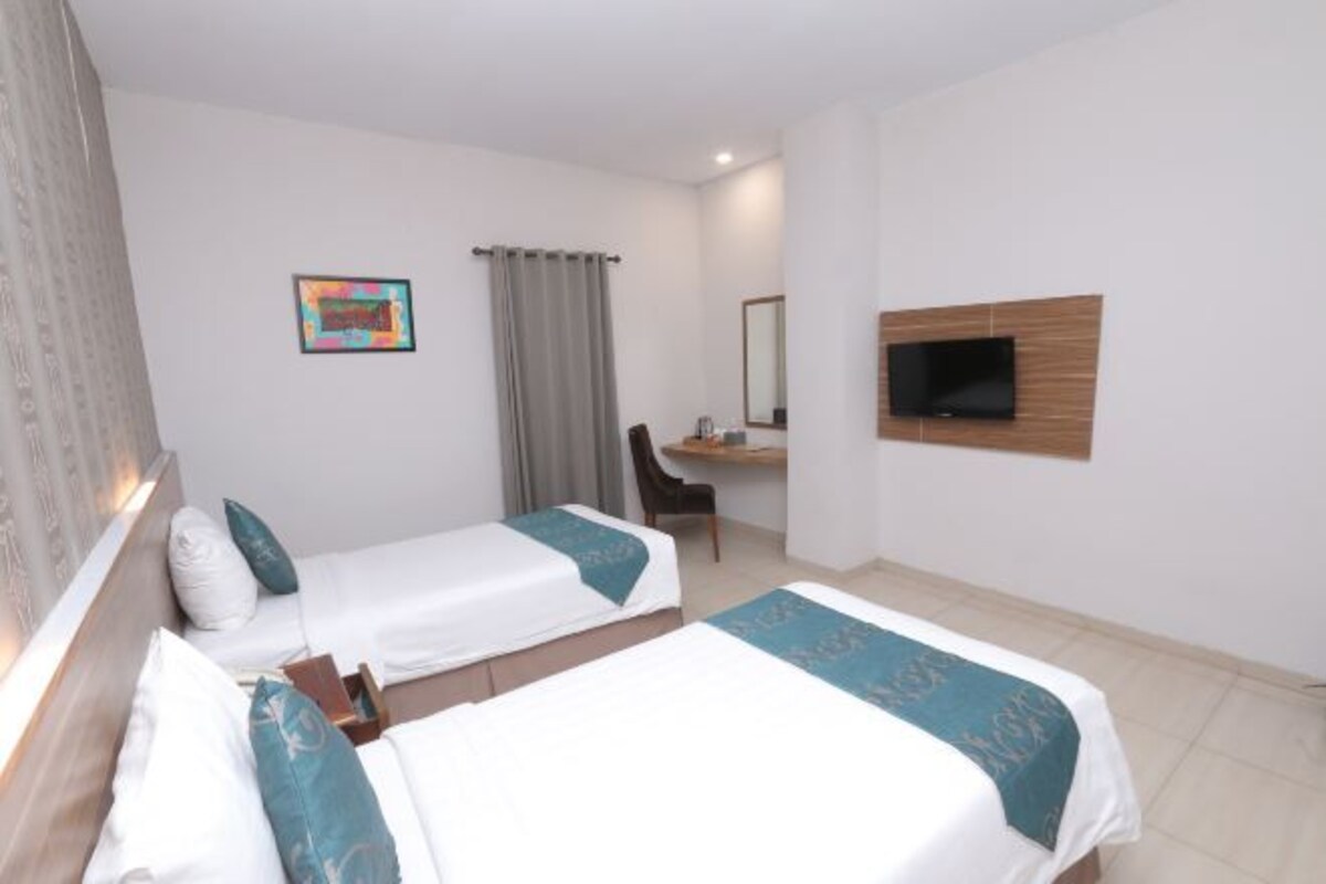 Habitación de hotel con dos camas, un escritorio, una silla, un televisor y un cuadro en la pared.