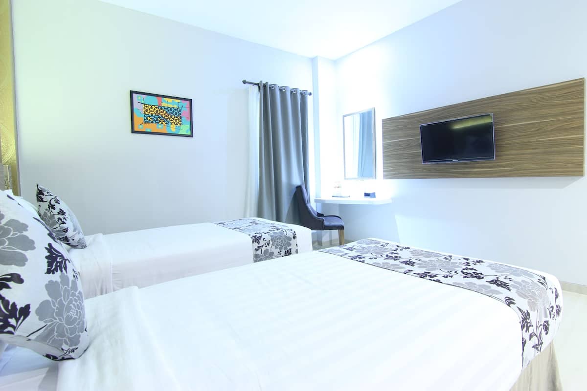 A hotel room with two beds, a TV mounted on the wall, a window with curtains, and a small desk.