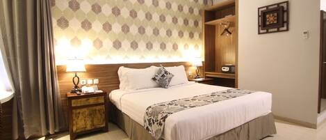 Cama bem arrumada com cabeceira de madeira, mesa de cabeceira com abajur e parede estampada.