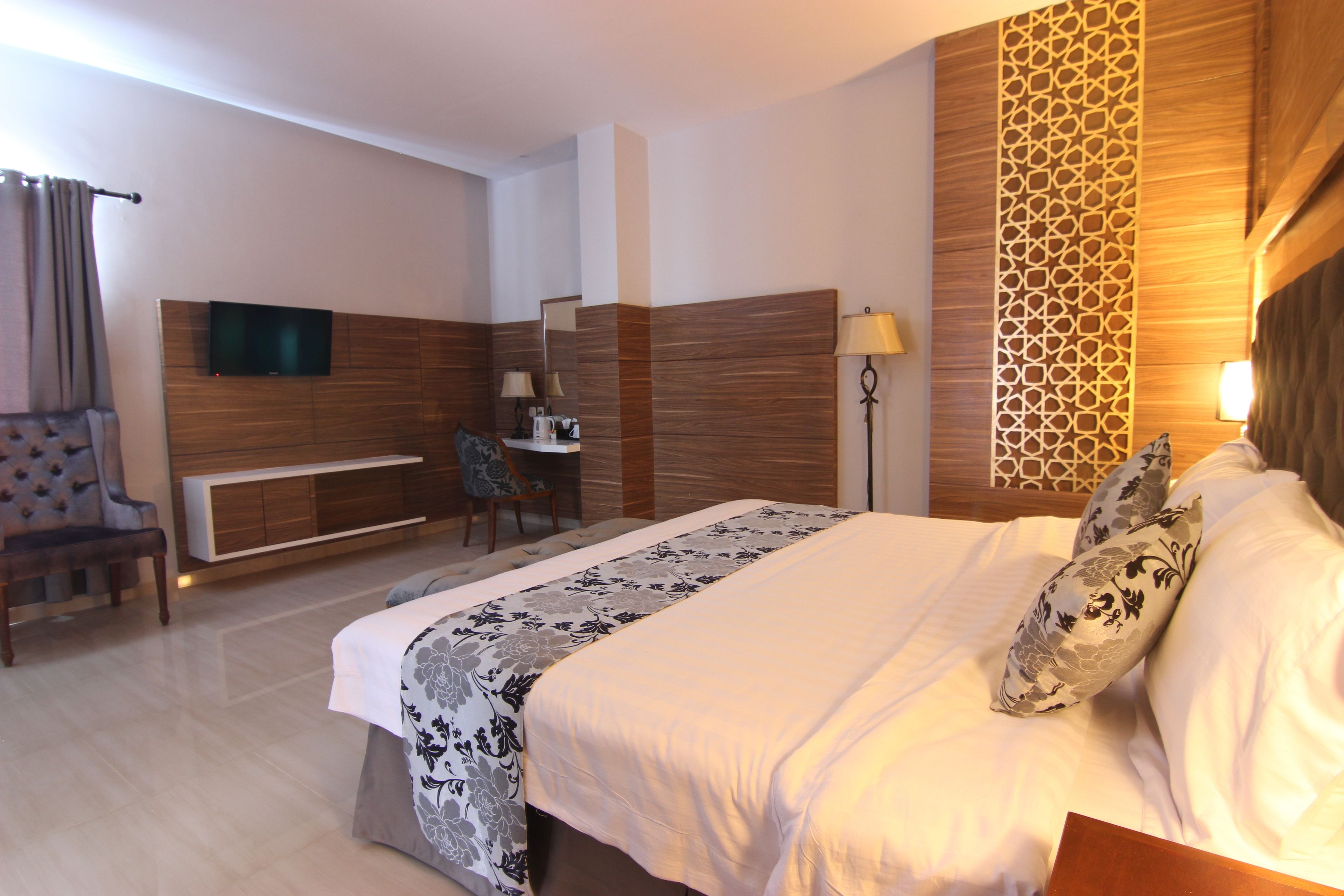 Quarto de hotel com uma cama grande, uma escrivaninha com cadeira, televisão fixada na parede e um painel decorativo.