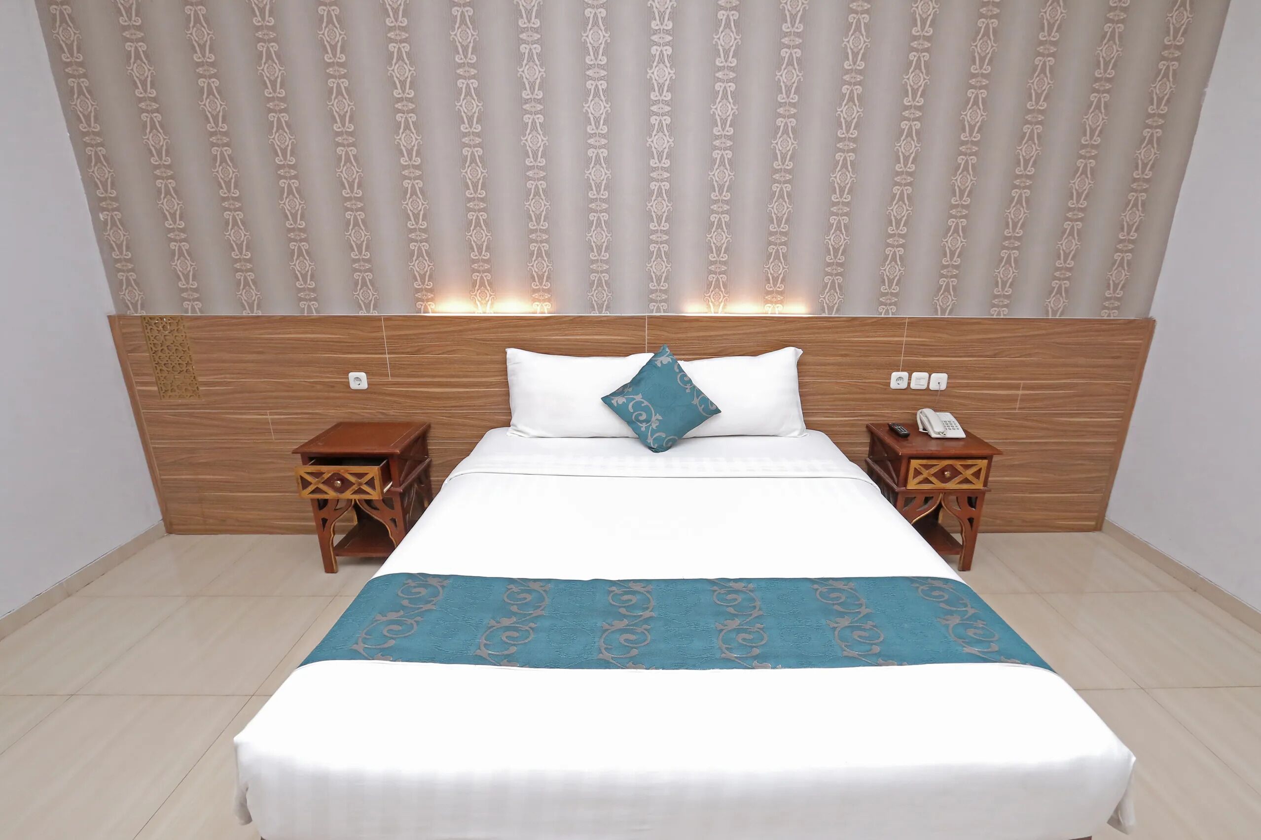 Un cuarto de hotel ordenado con una cama grande, dos mesitas de noche, un cabecero de madera y cortinas estampadas.