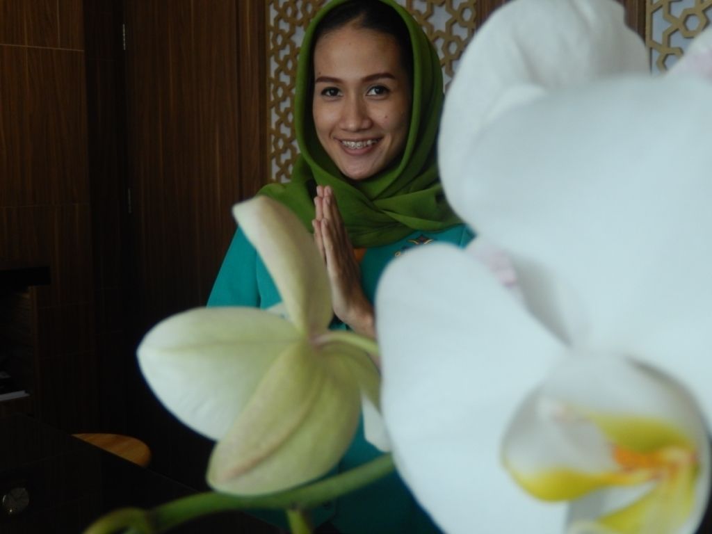 A person in a green headscarf sitting in front of a white orchid.